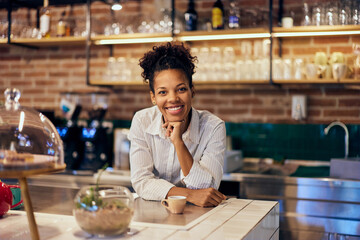A portrait of a smiling female barista, looking at the camera, dressed in a uniform.