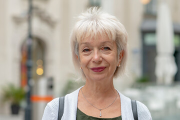 Street portrait of an elderly happy woman 65-70 years old on a blurred urban background of a...