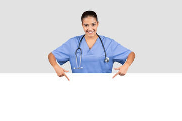 A smiling female doctor in blue scrubs leans over a blank banner