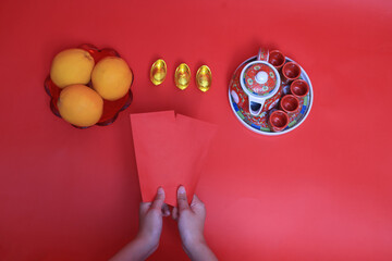 Chinese New Year girld hand hold red Angpao o with orange and tea set on red background