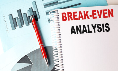 BREAK EVEN ANALYSIS text on a notebook with pen on a chart background