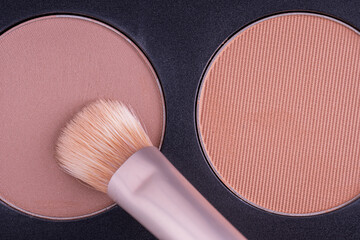 A palette with eye shadows and a makeup brush. Brush gains eyeshadows on pile to be used in make-up. Cosmetic swatch of eyeshadows, powder, bronzer or highlighter in brown-beige colors