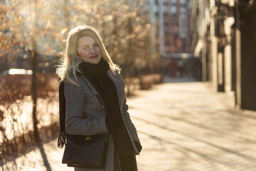 Obraz premium Beautiful young stylish blonde woman wearing long coat walking through the city streets. Trendy casual outfit. Street fashion. 
