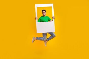 Full length photo of funny good mood pleasant man jumping with frame in hands make instant picture...