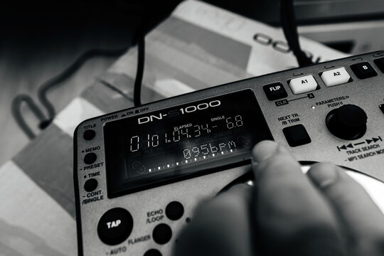 Paris, France - Oct 24, 2023: A male hand over the new Denon DN-S1000 DJ mixing equipment, testing at 095 BPM rhythm after unboxing, in a black and white scene