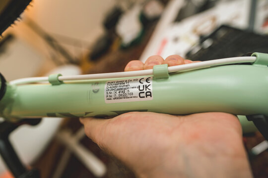Munich, Germany - Apr 8, 2023: Close-up view of a person hand assembling a Puky green bicycle frame, focusing on the tube with visible brand details and serial number.