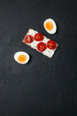 Ingredients for sandwich with boiled egg, cherry tomatoes, canned tuna, garlic and spices over black grunge background. High quality photo