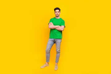Fototapeta premium Full size photo of confident serious guy wear stylish t-shirt denim pants holding hands folded isolated on yellow color background
