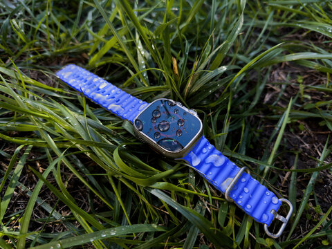 Paris, France - Sep 23, 2022: The image features an lost Apple Watch Ultra 2 lying on wet green grass, showcasing the watchs water-resistant capabilities following a rainfall - blue strap
