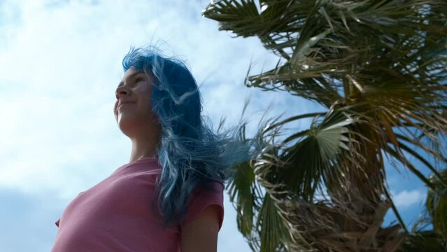 Wanderlust blue teen on beach. A pretty teen girl with blue hair have fun and waving hair by the palm tree on the beach in summer.