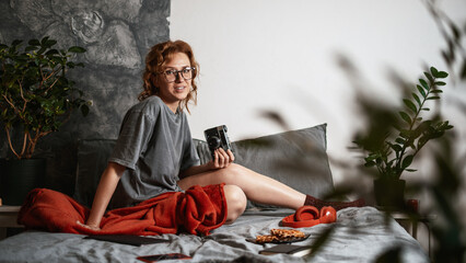 A young woman on a soft sofa at home takes pictures with an old vintage film camera. A full-length portrait.