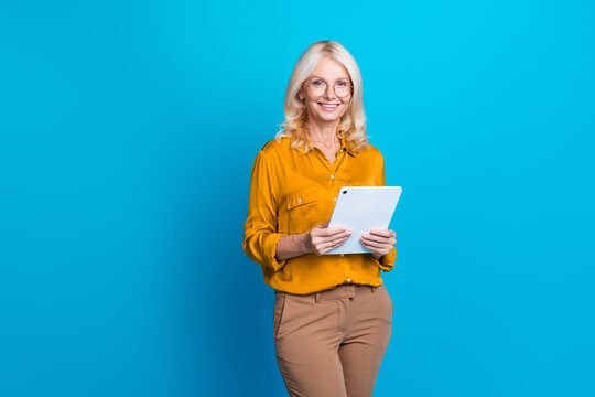 Photo portrait of attractive senior woman hold tablet read ebook wear trendy orange smart casual clothes isolated on blue color background - Powered by Adobe