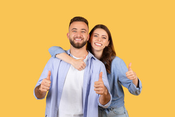 Enthusiastic couple giving thumbs up together on yellow background