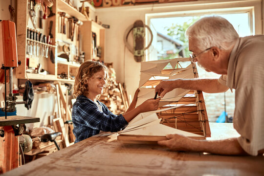 Grandfather and grandson working on a model boat in a woodworking workshop