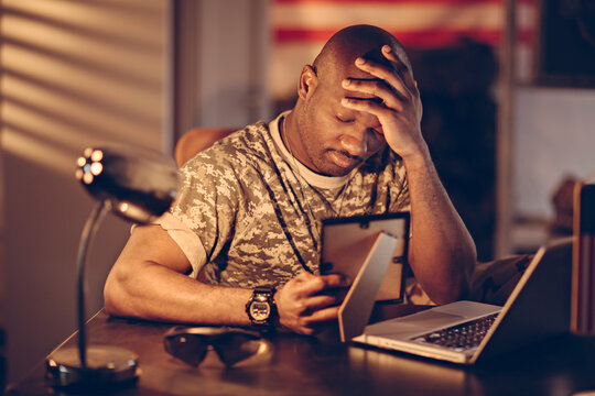 Stressed military man looking at photo while working late on laptop