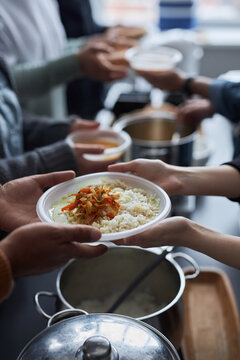 Vertical closeup of volunteers helping at soup kitchen and giving out hot meals, focus on hands holding plate with rice