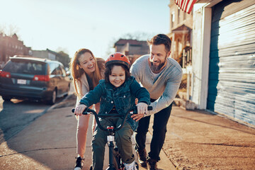 Family teaching child to ride bicycle in suburban neighborhood - obrazy, fototapety, plakaty