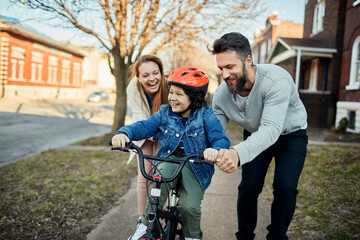Obraz premium Family teaching child to ride bicycle in suburban neighborhood
