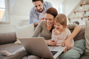 Happy family with young child using laptop on sofa at home