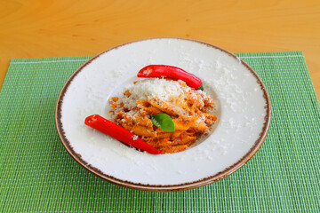 Pene alla arrabiata, Italian red sauce pasta served on a table in a plate with fresh grating of parmesan.