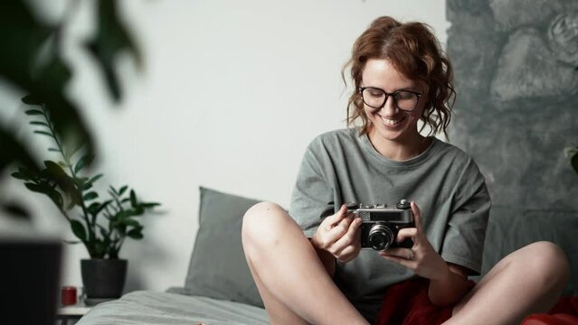 A young woman on a soft sofa at home takes pictures with an old vintage film camera. A full-length portrait.