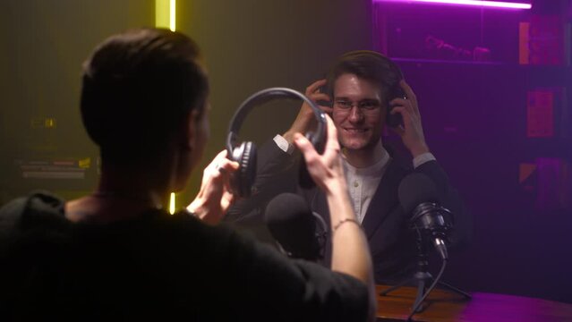 Close up portrait of a man journalist on a podcast communicates with a guest androgynous girl. People wear headphones. Streaming to a blog in a professional studio. The guy is a DJ on the radio