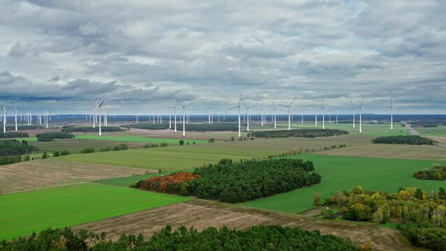 Drone approach to a wind farm during cloudy weather  between forests and fields