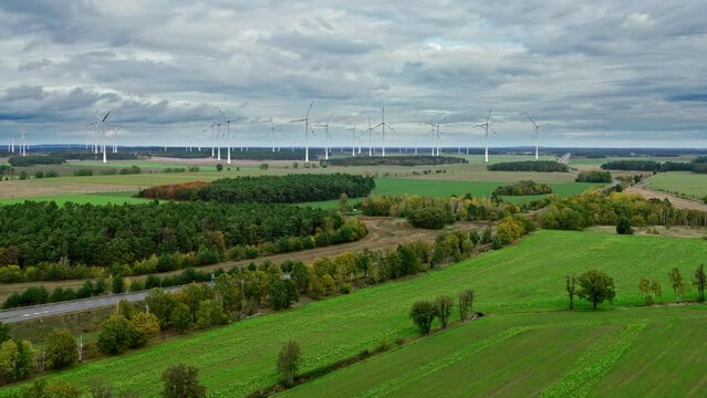Drone approach to a wind farm during cloudy weather between forests and fields