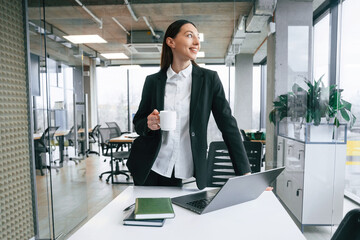 Standing by the table. Businesswoman is indoors in the office