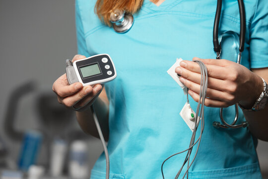 Doctor showing ECG holter monitor to patient in pediatric clinic. Holter monitoring device in a doctor hands before a diagnostic. Preparation for a heart rhythm diagnistic. Professional medicine.