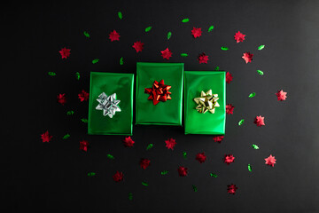 Creative handmade christmas green and silver paper gift boxes with decor on black background, top view.