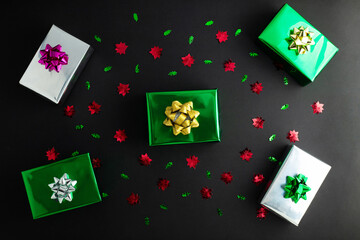 New Year concept. Top view photo of stylish green giftbox with golden ribbon bow and Christmas decorations colored gift boxes with confetti on isolated black background with copyspace