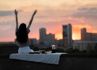 young girl on a city rooftop having a picnic and watching gorgeous sunset