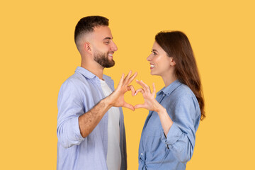 Couple making heart shape with hands, sharing joyful moment on yellow