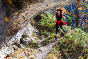 Naklejka na ściany i meble Curly Long Hair Gritty Woman Running Wild Downhill on an Alpine Mountain Trail Carefree