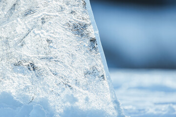 Transparent ice shard stands in a snowdrift on a sunny winter day