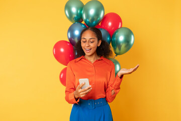 Fototapeta na wymiar black girl holding smartphone posing with bunch of balloons, studio