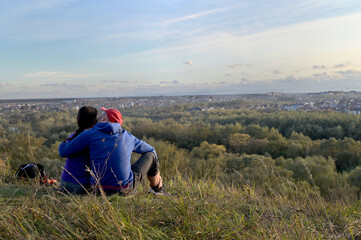 Fototapeta na wymiar A young couple in love are kissing sitting on a hill near the city ​