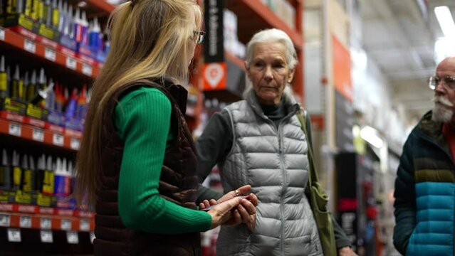 Mature woman with elderly man and woman trying to find and compare products in hardware store using smart phone in slow motion.