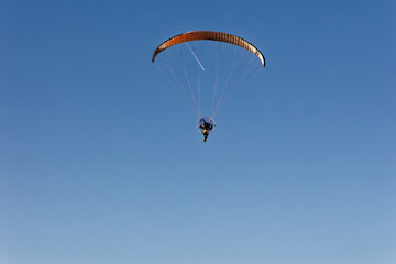 Motorized paraglider flying against the blue sky with clouds, outdoor activity, extreme sports, extreme sports, paraglider flying in the sun in the sky. The sport of paragliding