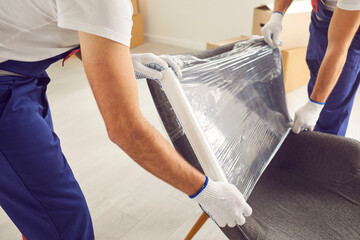 Skilled movers are captured in a close up shot, wrapping an armchair in protective stretch film...