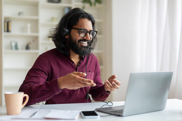 Portrait Of Smiling Indian Man In Headset Making Video Call On Laptop