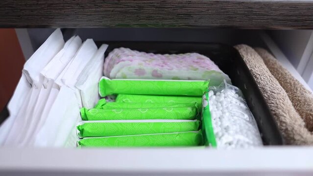 Sanitary napkin, tampon and cotton plant flower. Women hands pull out drawer containing hygiene products to help with menstruation. Cotton flower symbolizes absence of plastic. Made from eco materials