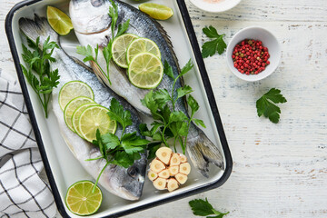 Raw fresh. Fresh raw dorado with lemon, lime, parsley and salt on old wooden white background ready for cooking. Sea bream, dorado. Seafood, healthy food. Top view. Long banner format.