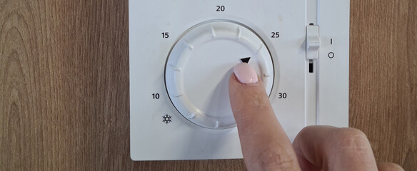 Person regulates the air temperature in room at home or in office using remote control on wall