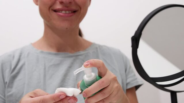 millennial young woman is doing at home facial procedure, remove makeup with hydrophilic oil and cotton disk,massaging face with roller and cleaning with ultrasound device.girl using mirror.