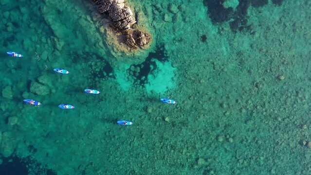 Aerial view of people with paddleboard in the bay along the cliffs, Platja de Cala Xarraca, San Juan Bautista, Balearic Islands, Spain.