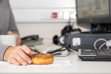 A man's hand holds a donut in the workplace. The concept of a workplace break in the office.