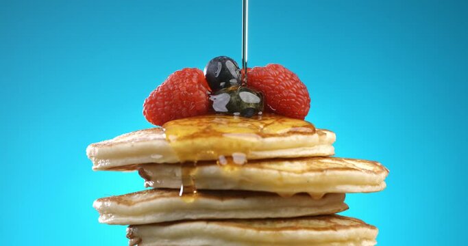 Super slow motion macro of honey or caramel syrup is covering on sweet delicious dessert pancakes with berries isolated on soft colorful background at 1000 fps.