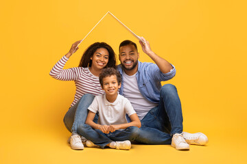 Happy Black Family With Little Son Sitting Under Symbolic Carton Roof